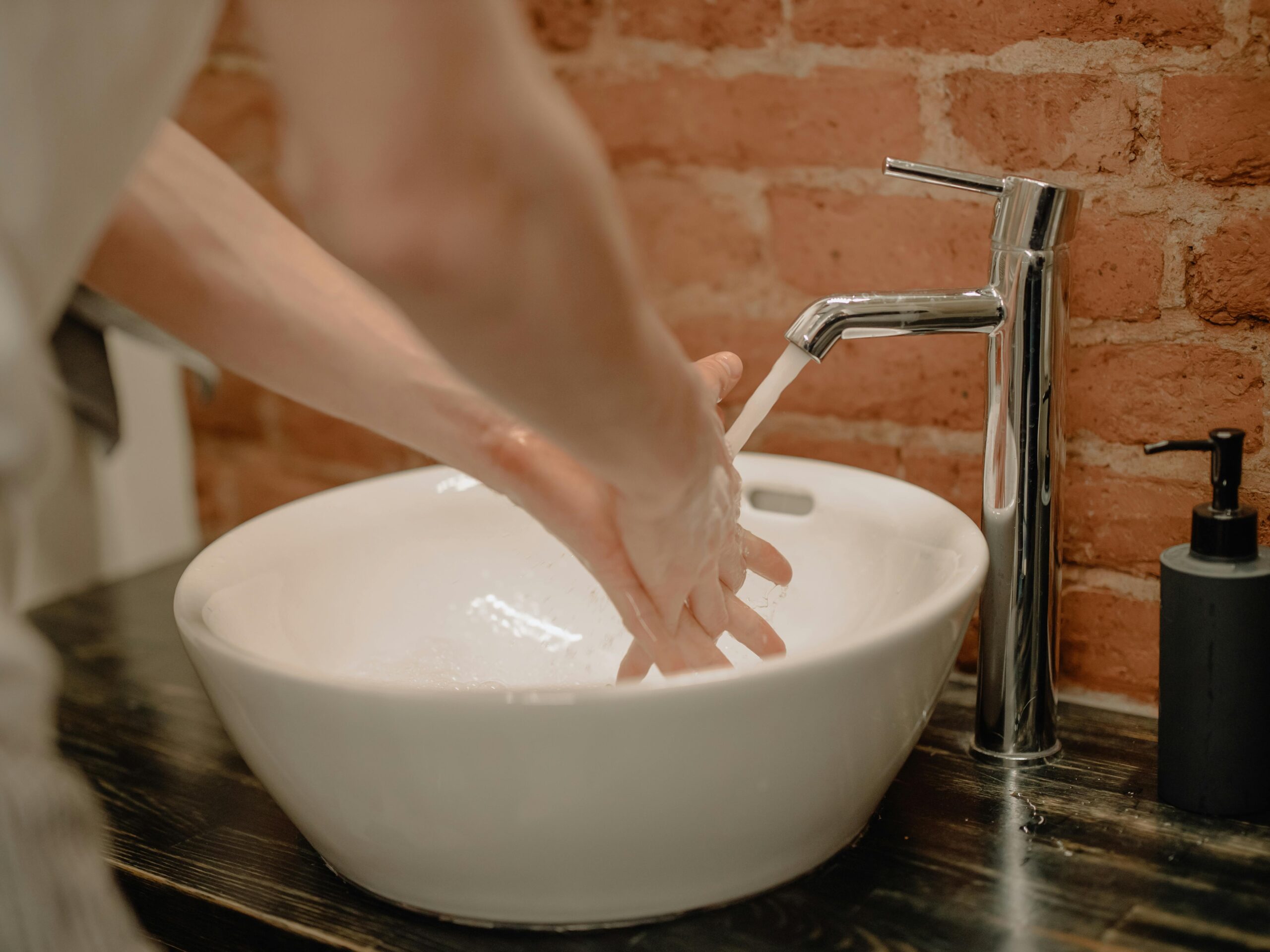 Hands being washed under a modern faucet in a bathroom, emphasizing hygiene and cleanliness.